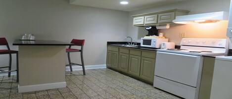A kitchen with a central island, two bar stools, a microwave, a stove, and light green cabinets.