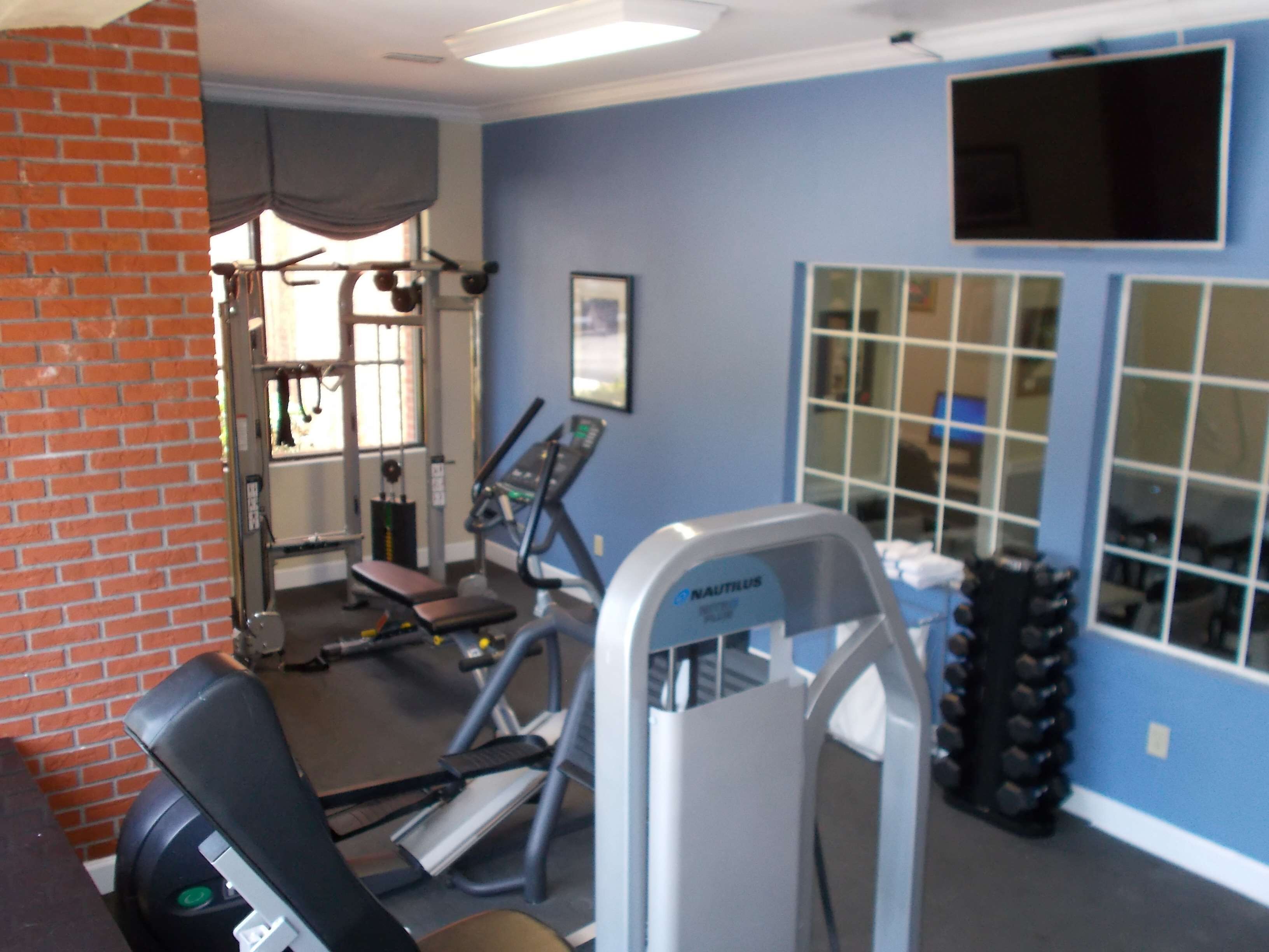 Une salle de sport équipée de matériel d’exercice, avec un mur en briques et une grande fenêtre.