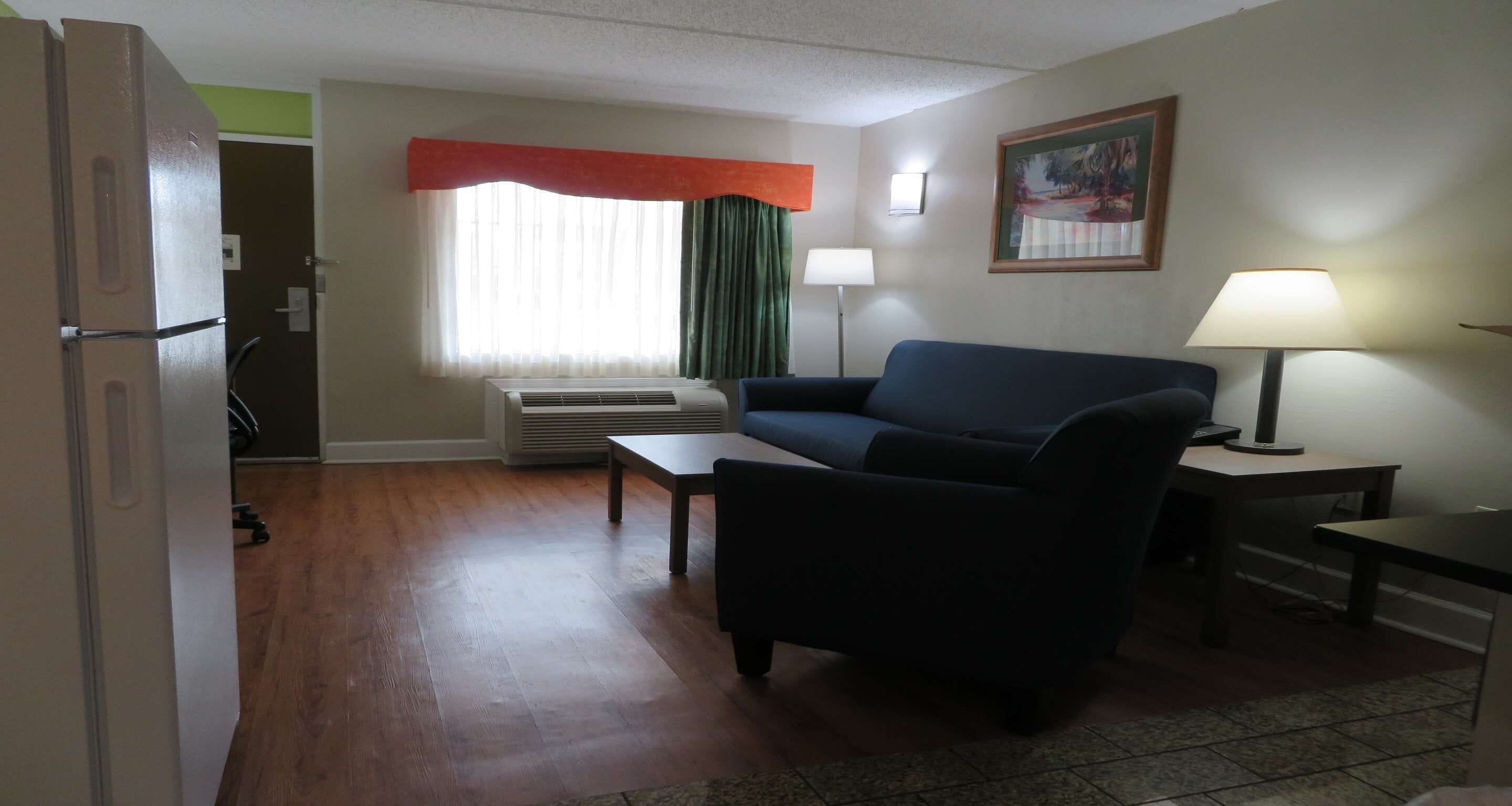 A living room with a sofa, a coffee table, a lamp, a painting on the wall, and a window with curtains.
