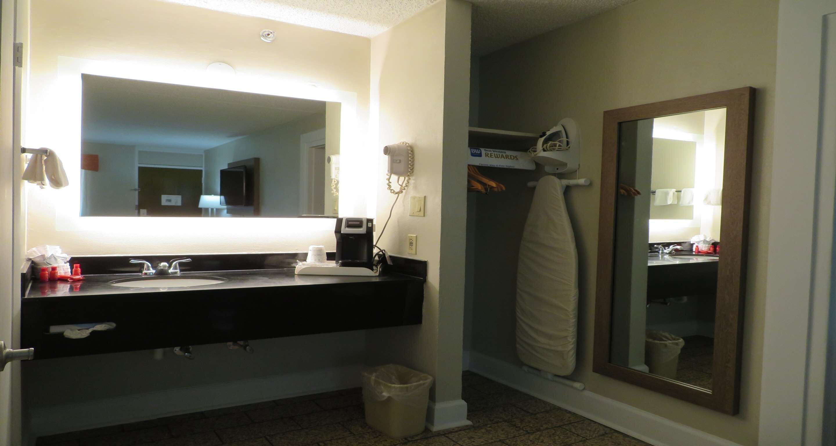 Une salle de bain d’hôtel avec un grand miroir, un lavabo noir, un sèche-cheveux et un porte-serviettes.
