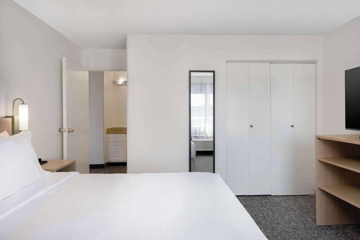A hotel room with a bed, a TV on a stand, a desk with a lamp, and a wardrobe.