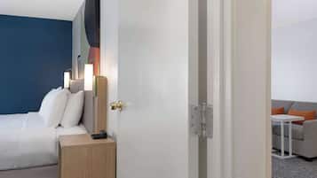 A hotel room with a bed, bedside table, and a small table with a lamp.