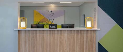 A reception desk with a wooden panel design, two illuminated lamps, and a large abstract artwork on the wall.