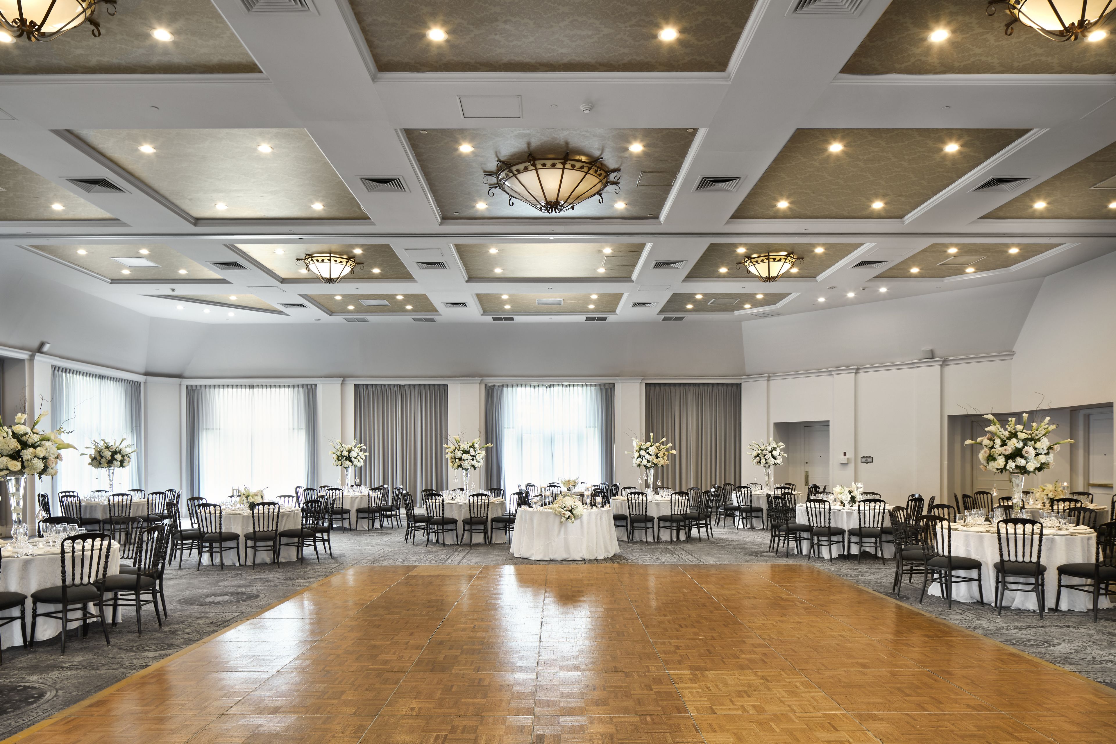 Un amplio salón de banquetes con varias mesas redondas, sillas y una pista de baile central.