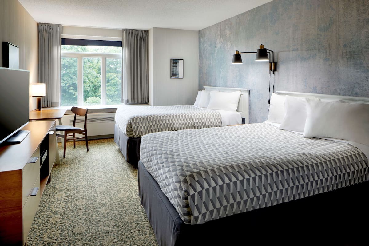 Een hotelkamer met twee bedden, een bureau, een stoel, een televisie en een raam met gordijnen.