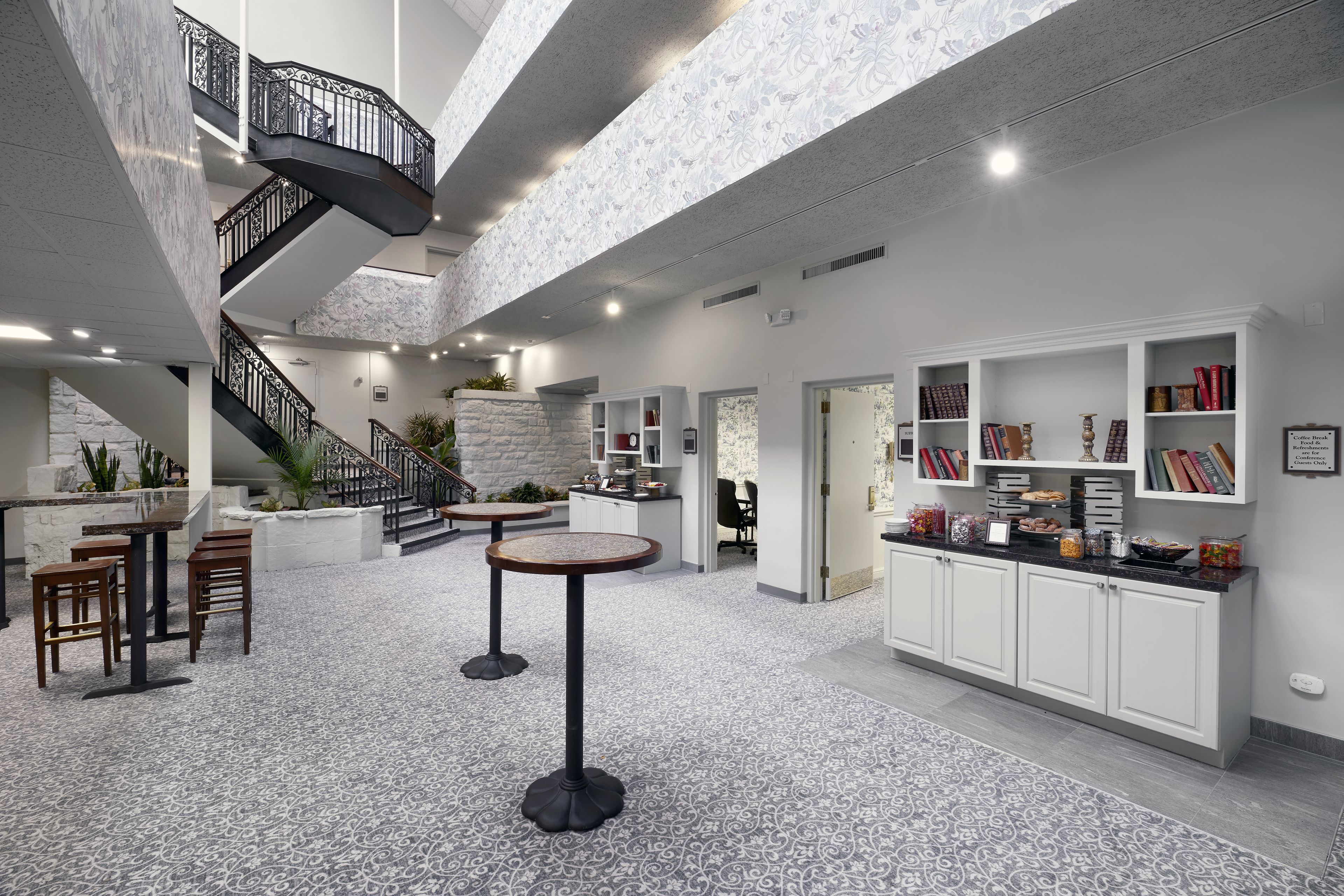 Een ruime lobby met een marmeren vloer, een centrale trap en een zithoek met ronde tafels.