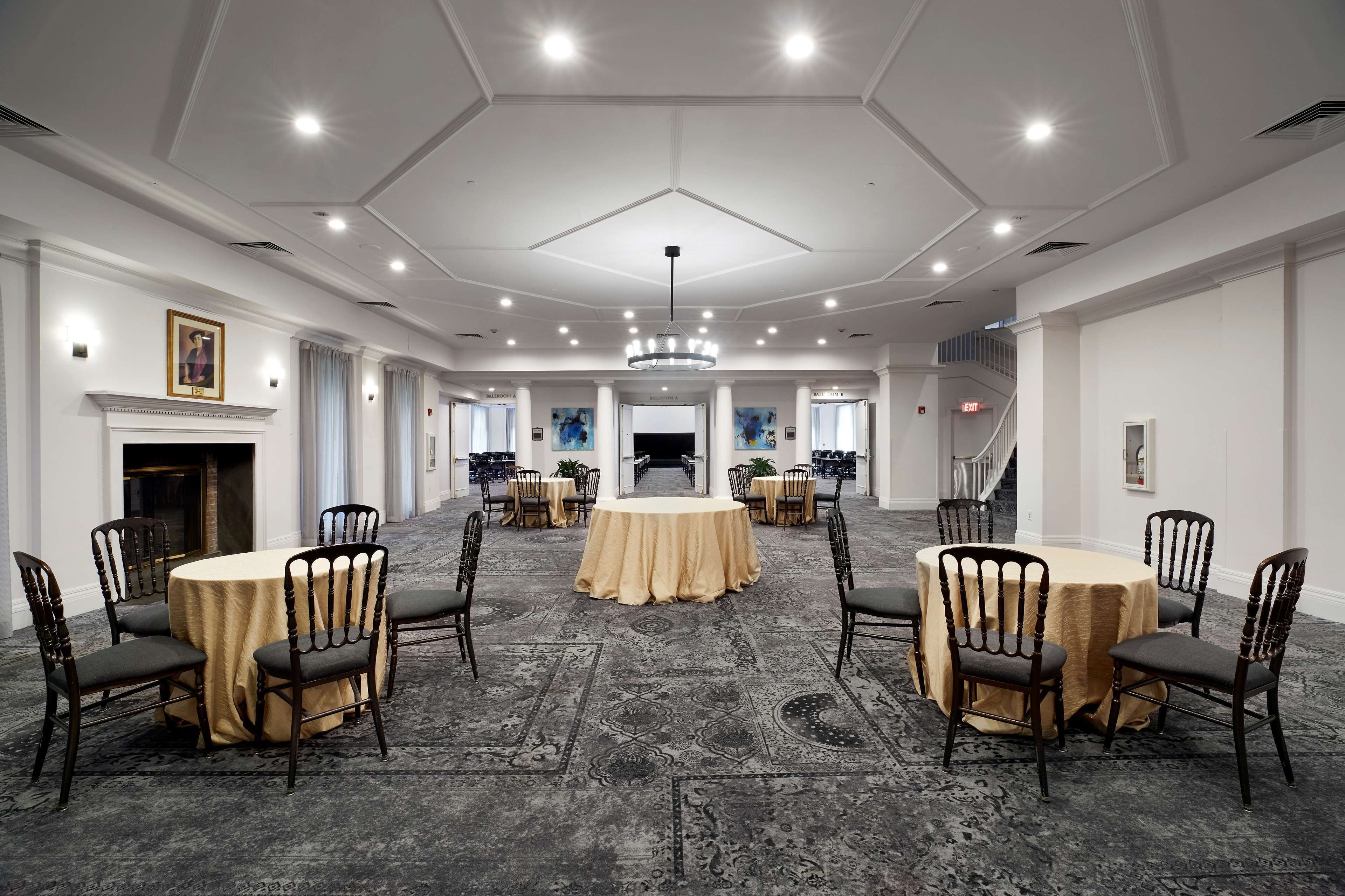 A spacious conference room with round tables and chairs, a chandelier, and a patterned carpet.