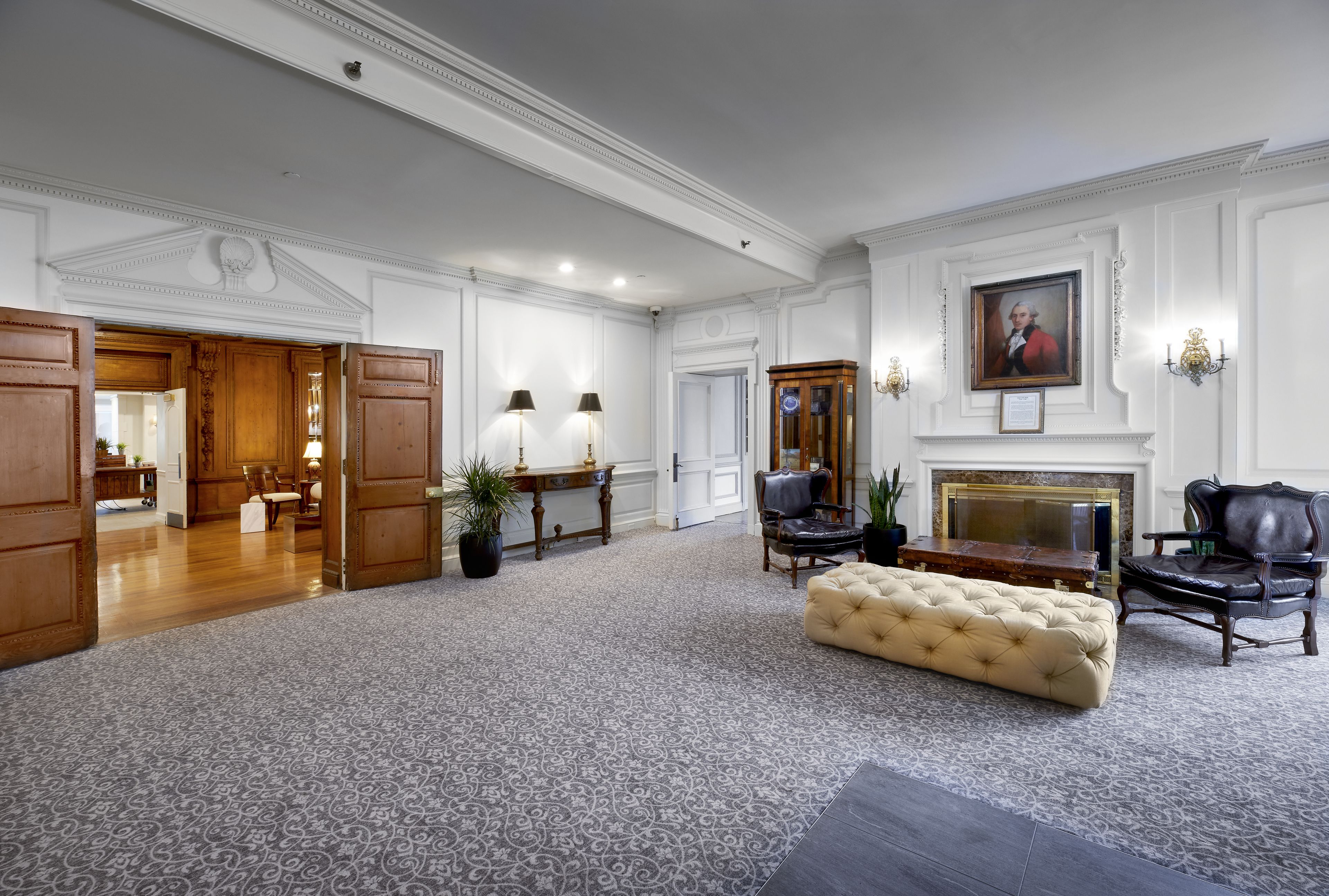 Une pièce spacieuse avec un tapis à motifs, un grand pouf, une cheminée et des meubles classiques.