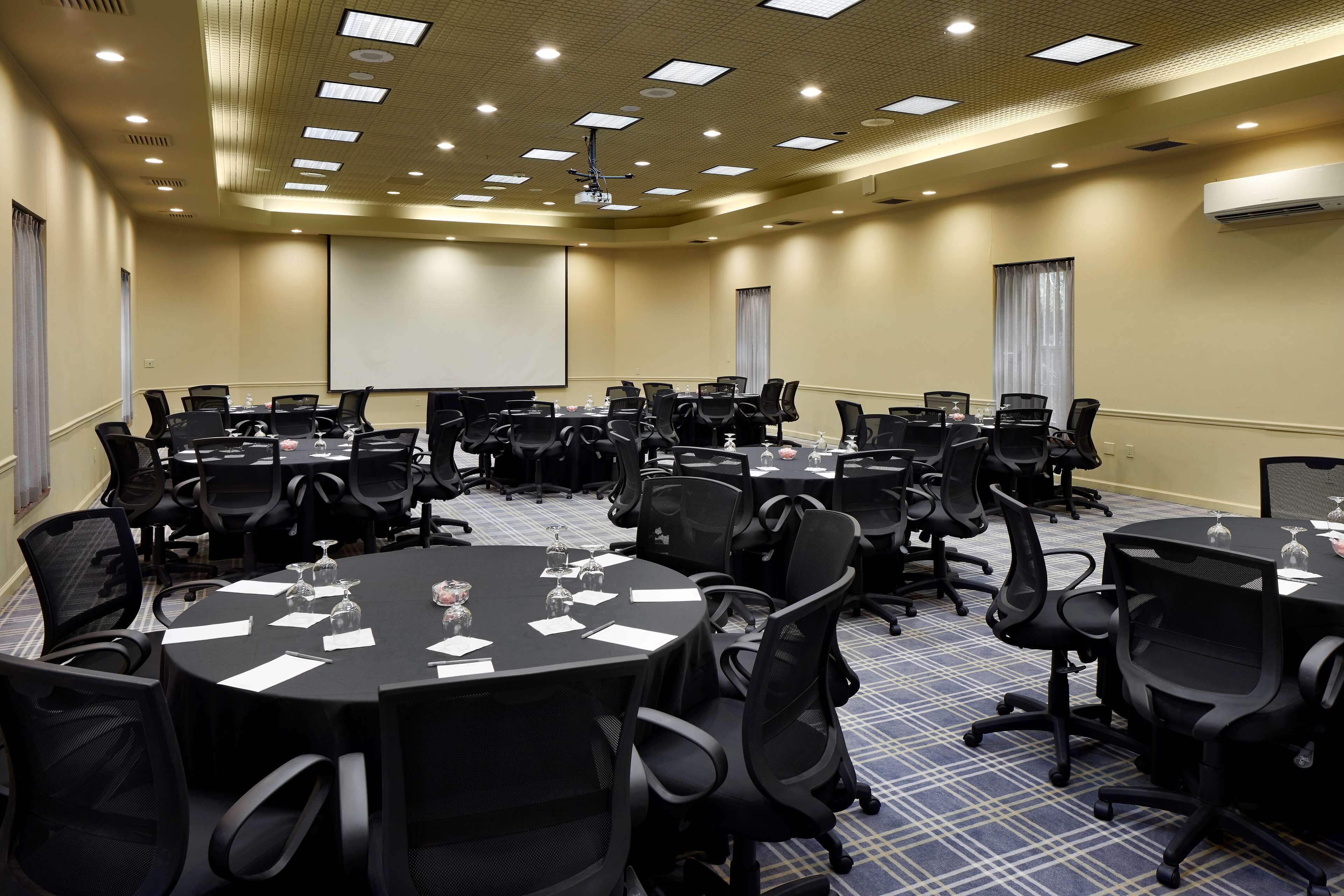 A conference room with multiple tables and chairs, a projector screen, and an air conditioning unit.