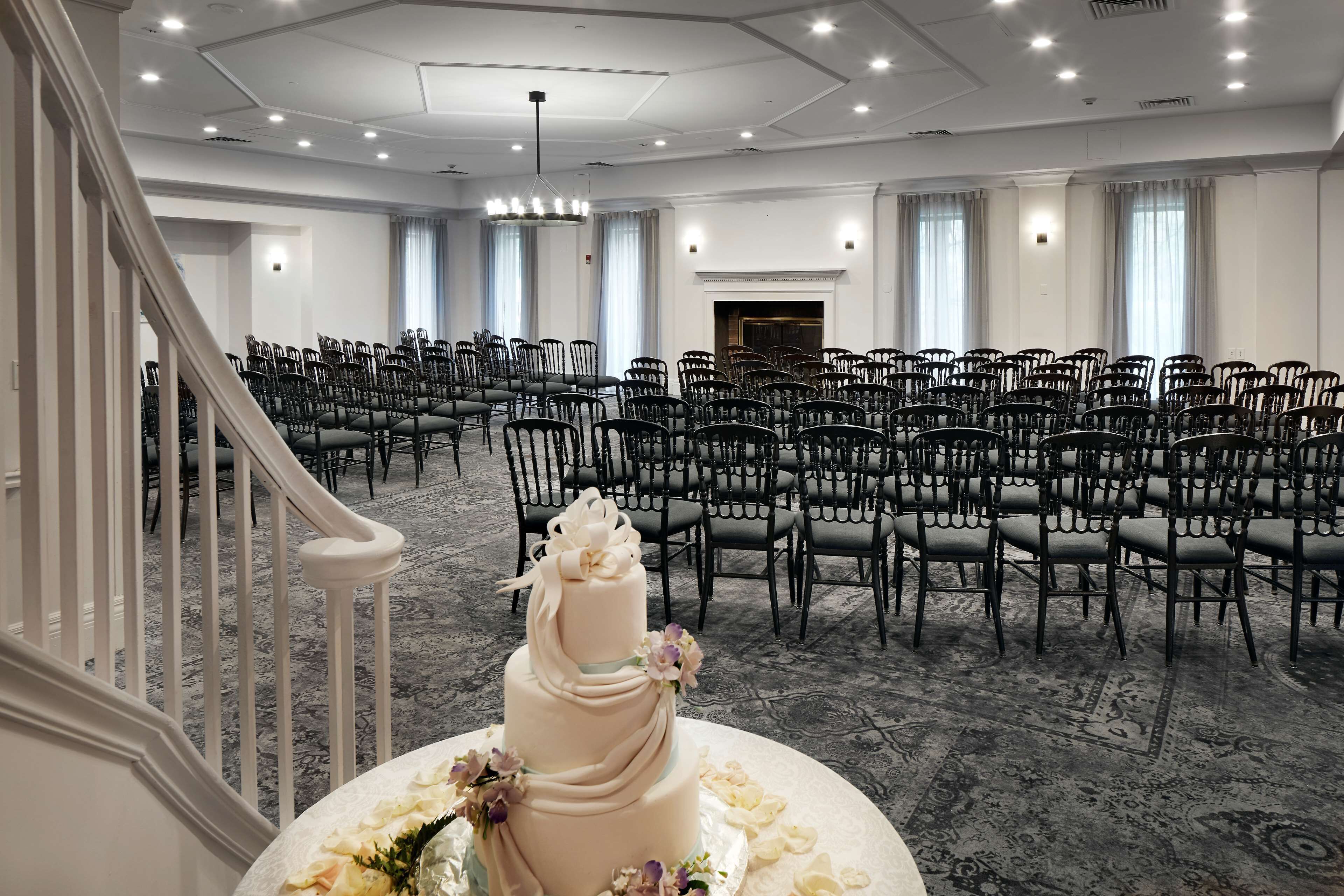 Une grande salle de conférence, bien éclairée, avec des rangées de chaises, un magnifique escalier et un gâteau décoratif posé sur une table.