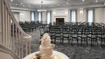 A large, well-lit conference room with rows of chairs, a grand staircase, and a decorative cake on a table.