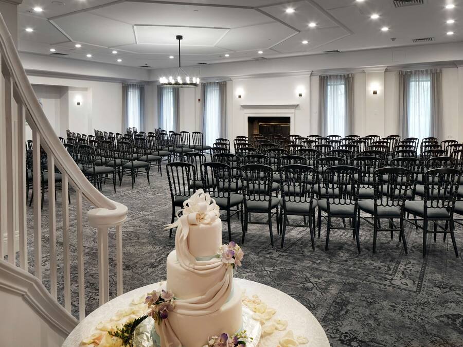Een ruime, goed verlichte conferentiezaal met rijen stoelen, een statige trap en een decoratief taartje op een tafel.