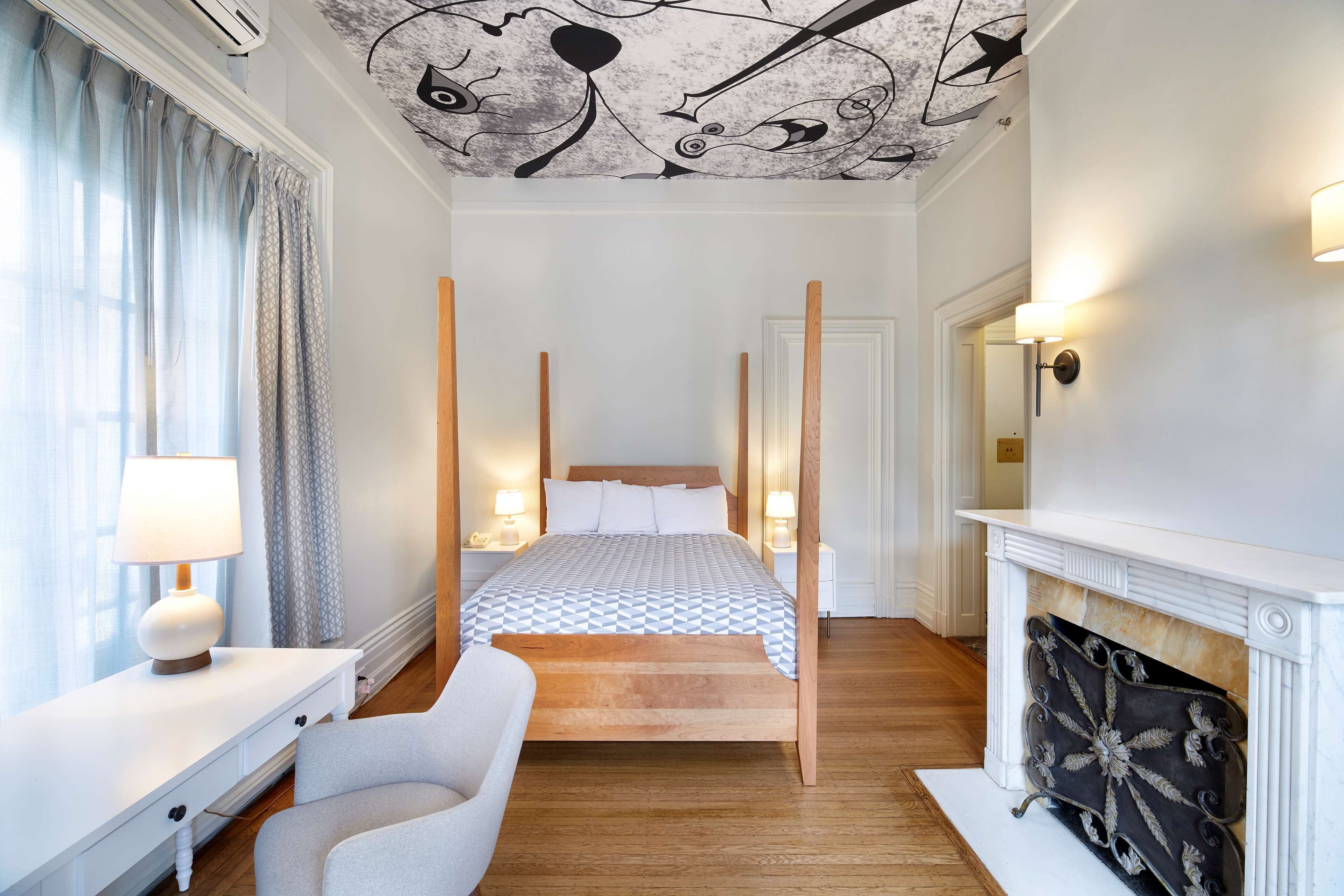 Quarto com cama de dossel, luminárias de cabeceira, mesa de cabeceira branca, uma cadeira e lareira.