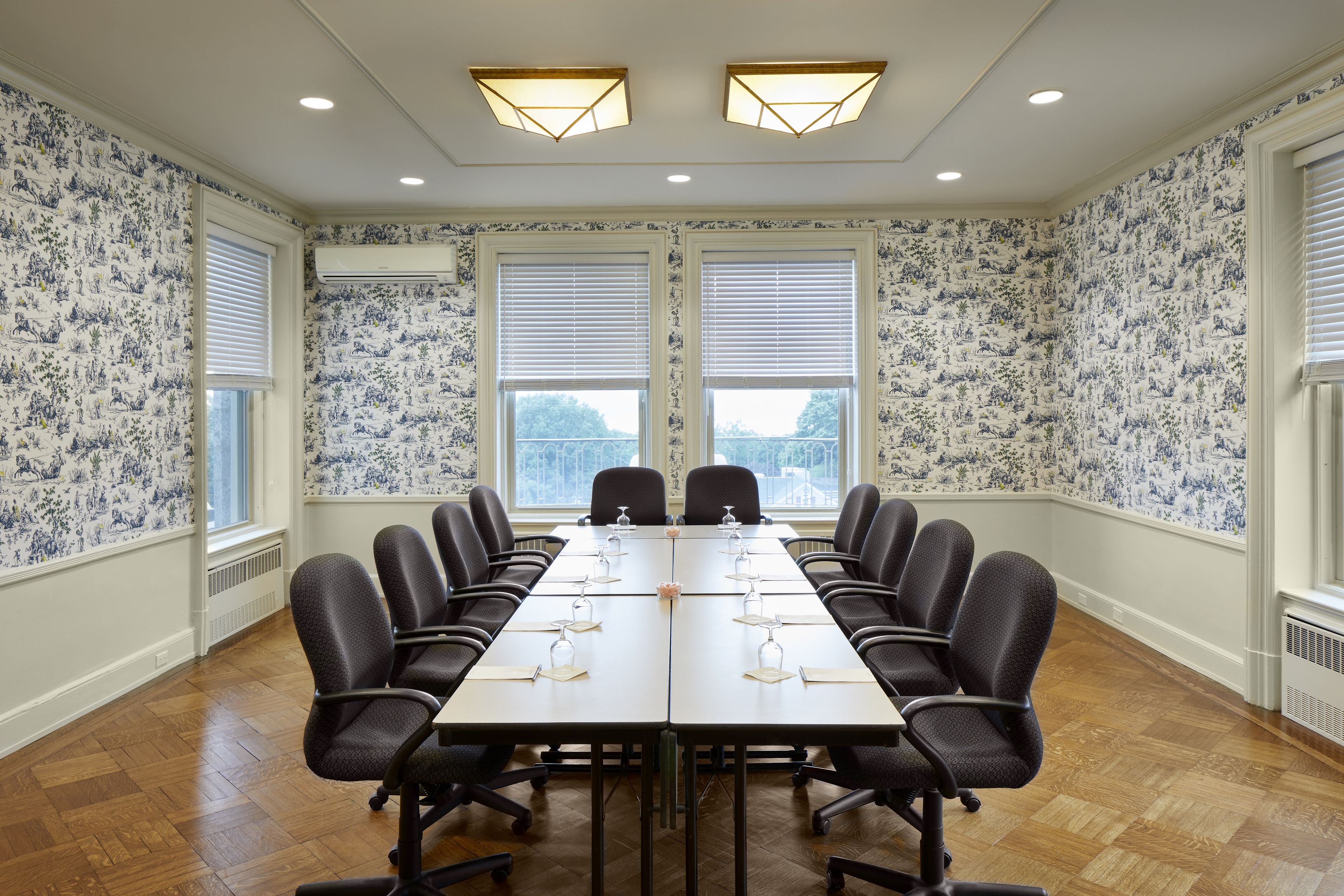 A conference room with a long table, chairs, and two windows with blinds.