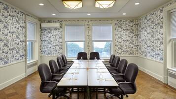 A conference room with a long table, chairs, and two windows with blinds.