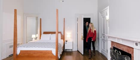 Ein Zimmer mit einem Himmelbett, Holzboden, Kamin und einer Tür zu einem weiteren Raum.
