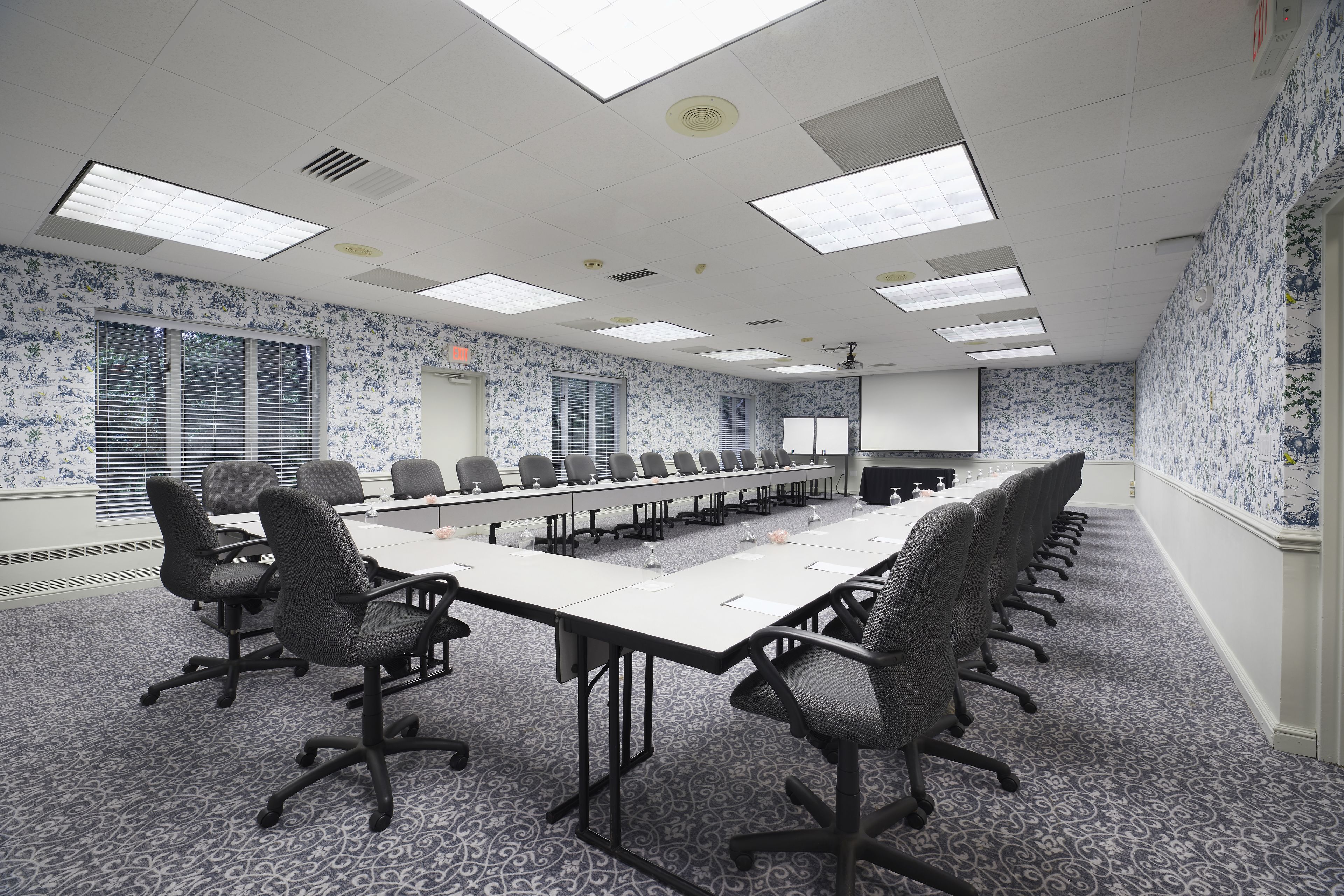 A conference room with a long table, multiple chairs, patterned carpet, and patterned wallpaper.