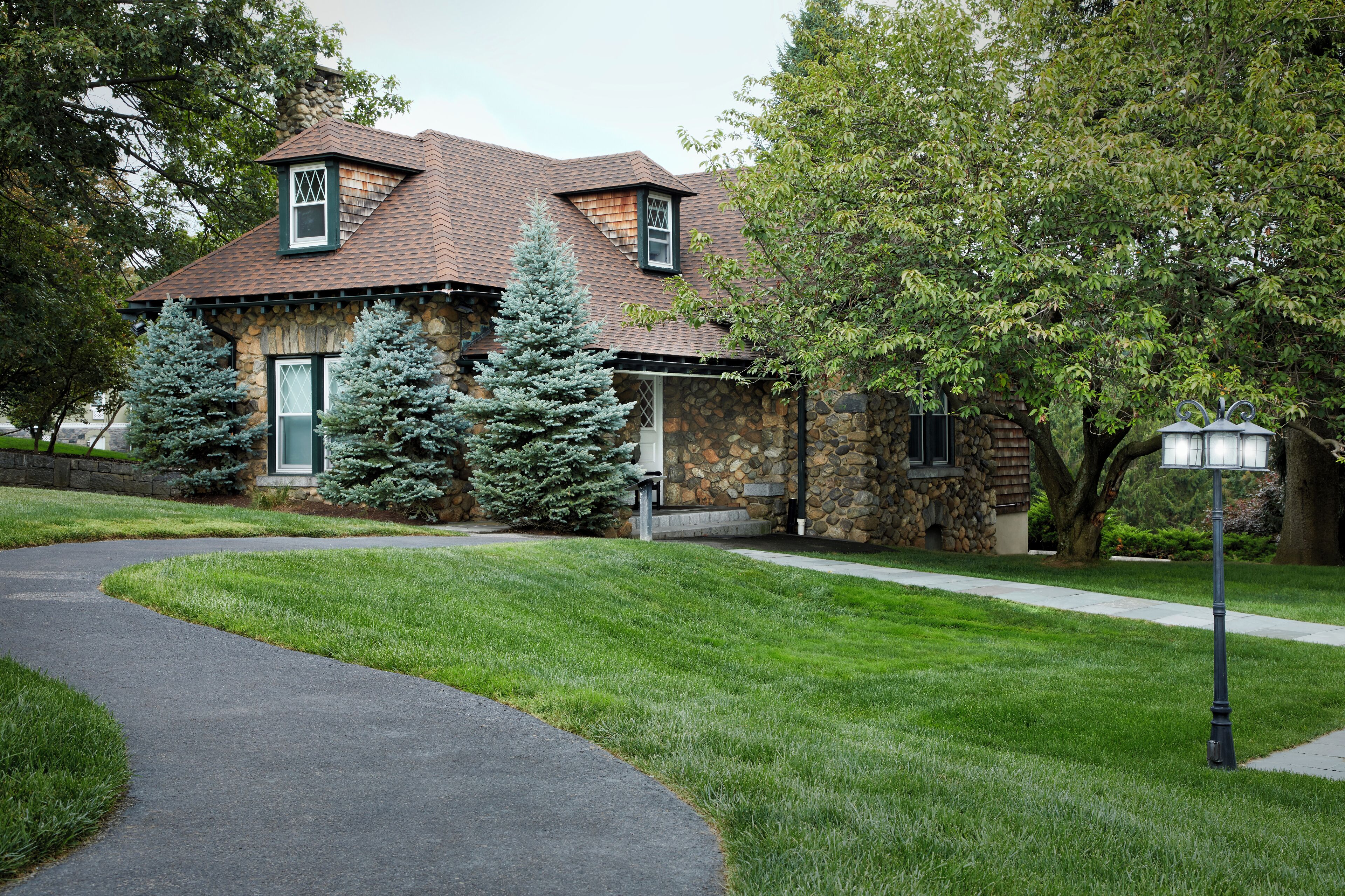 A stone house with a sloped roof, a front porch, and a pathway leading to the entrance.