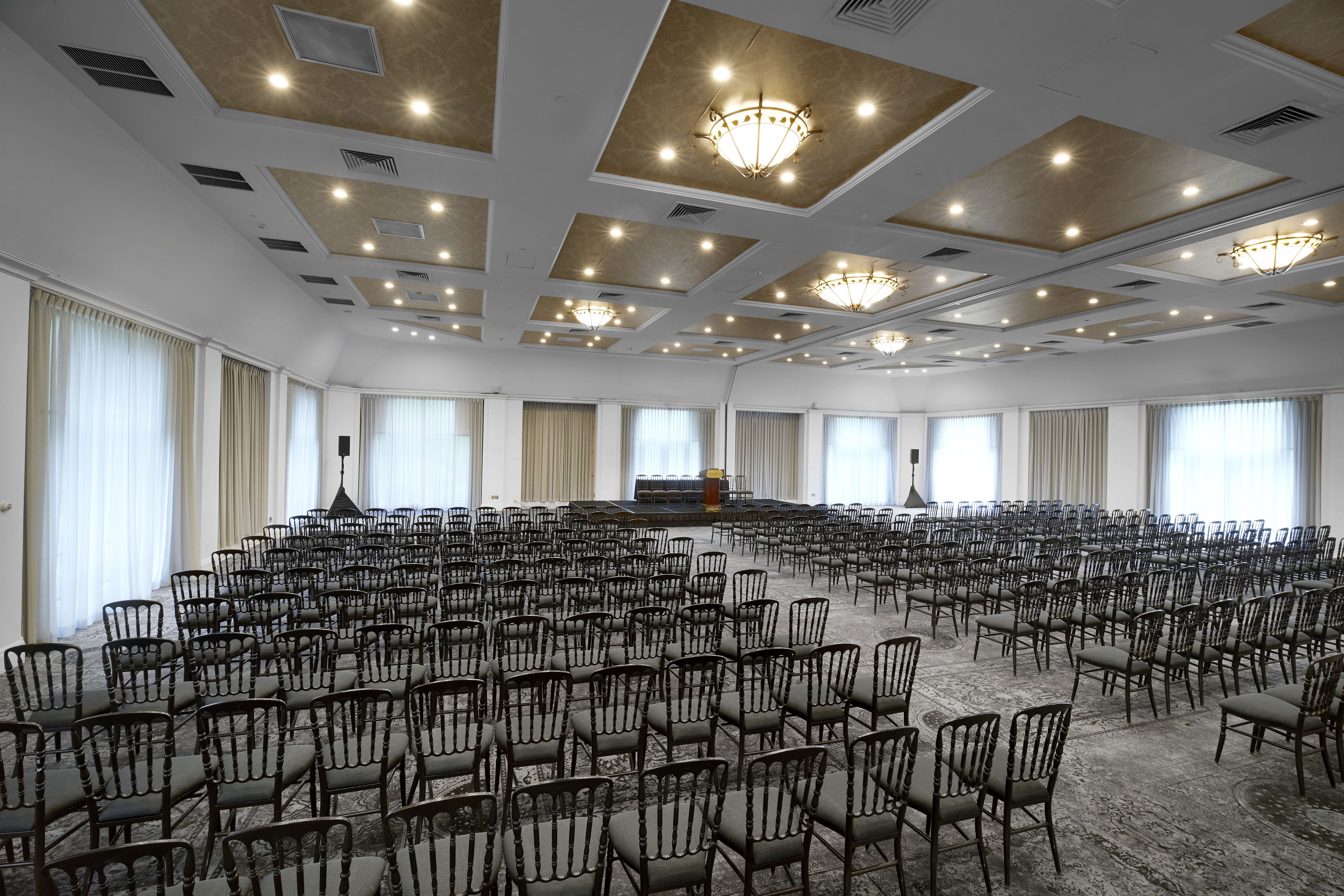 A large conference room with rows of chairs, a stage, and a chandelier.