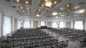 A large conference room with rows of chairs, a stage, and a chandelier.