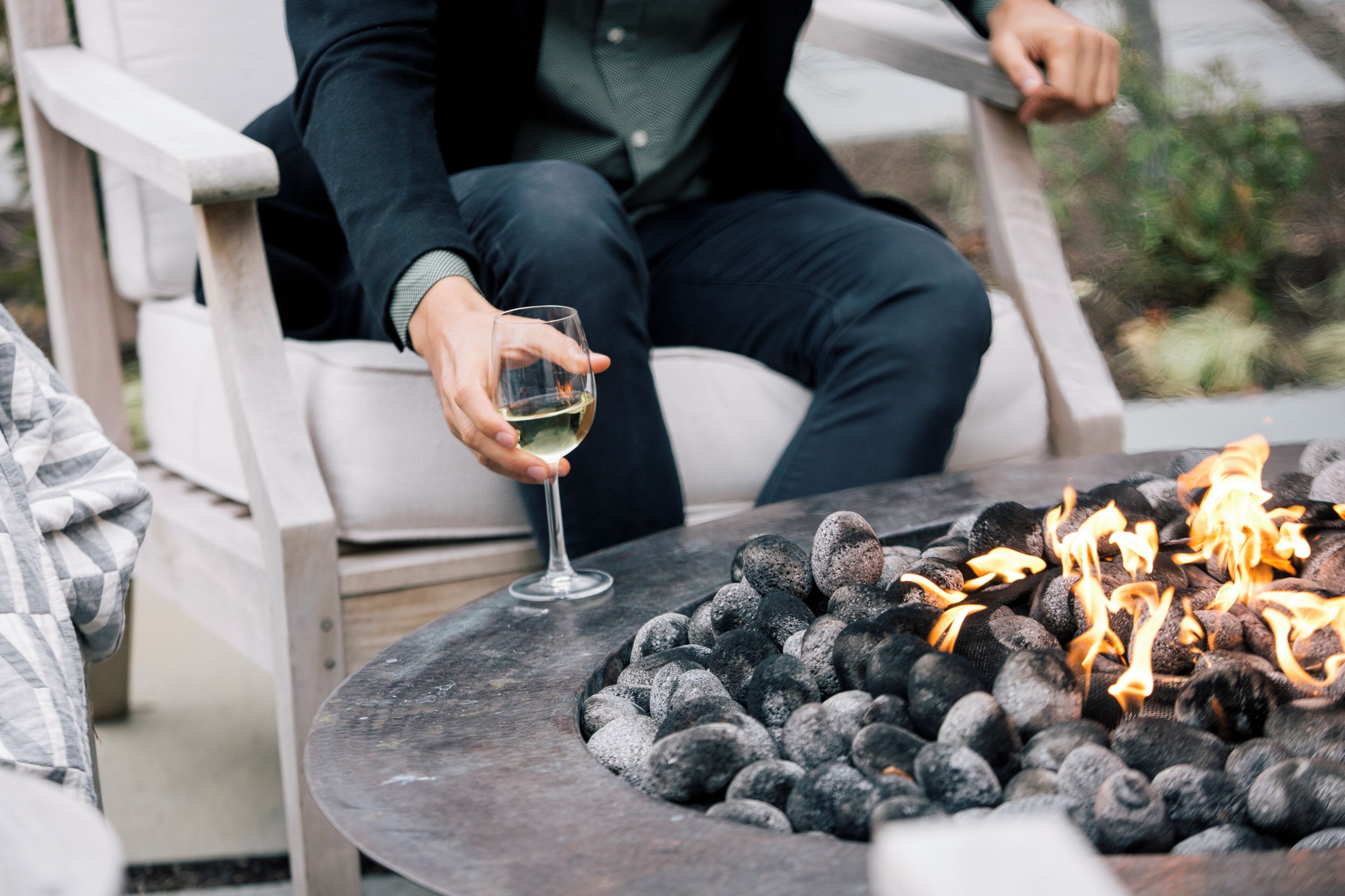 A person seated at a table with a fire pit in the foreground.
