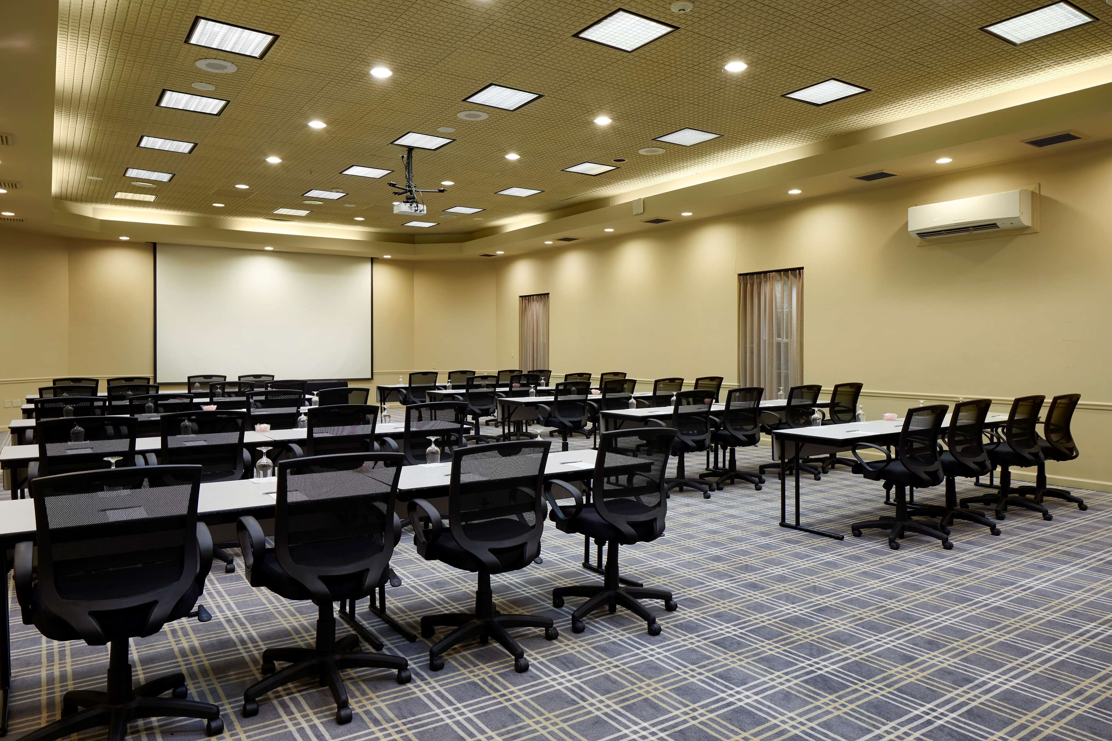 A conference room with multiple tables and chairs, a ceiling with recessed lighting, and an air conditioning unit on the wall.