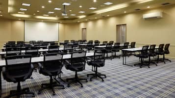 A conference room with multiple tables and chairs, a ceiling with recessed lighting, and an air conditioning unit on the wall.