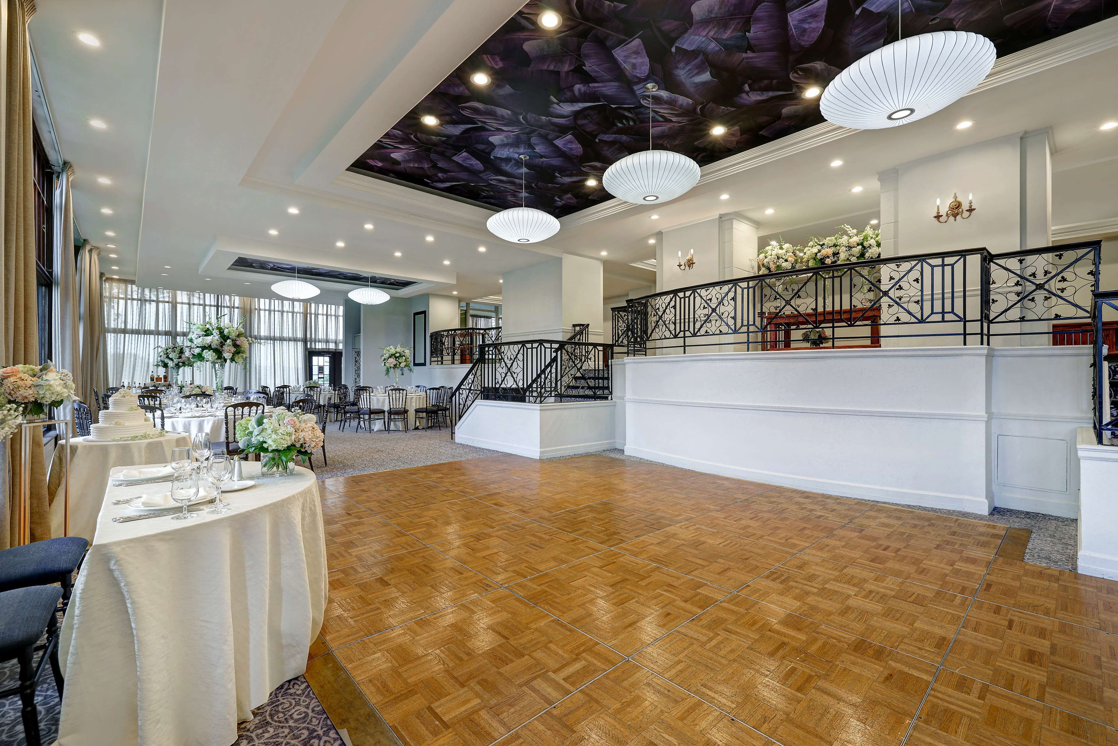 A spacious hall with a wooden parquet floor, white walls, and a ceiling with a leaf pattern.