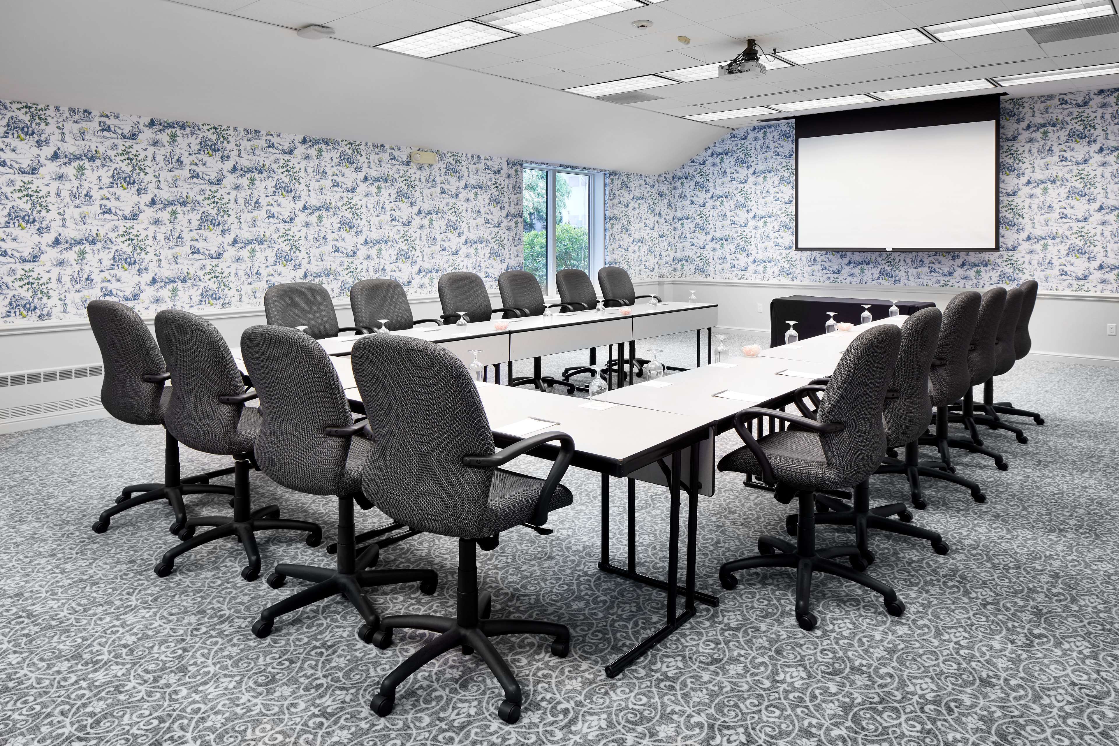 Un salón de conferencias con una larga mesa, varias sillas, una pantalla de proyector y un papel tapiz estampado.