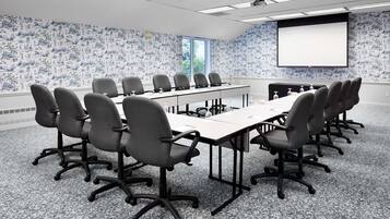 Un salón de conferencias con una larga mesa, varias sillas, una pantalla de proyector y un papel tapiz estampado.