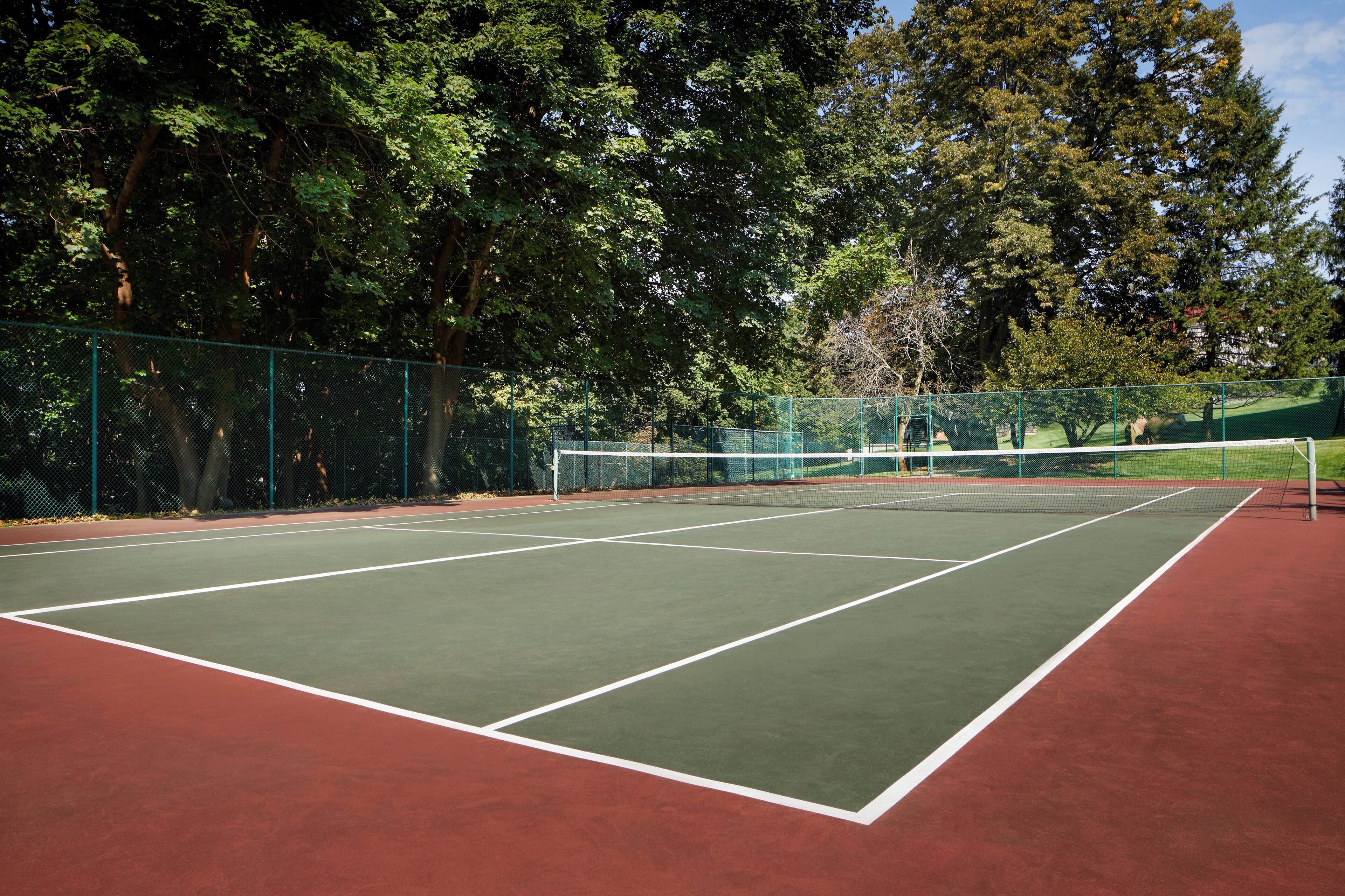 Un court de tennis en plein air avec une surface verte et rouge, entouré d’arbres.