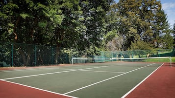 Una cancha de tenis al aire libre con superficies verdes y rojas, rodeada de árboles.