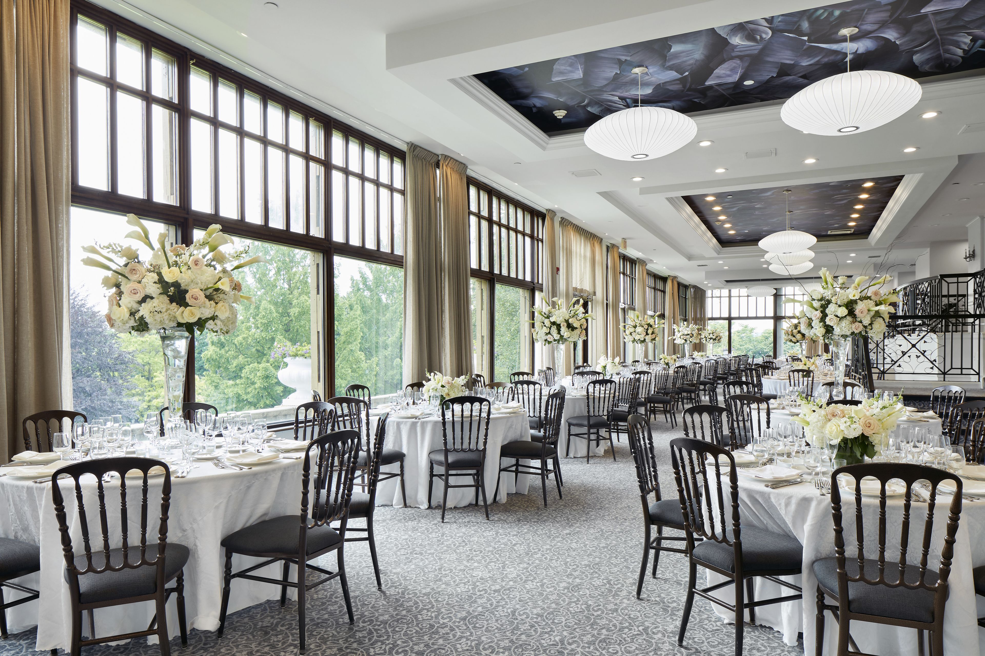 A banquet hall with multiple round tables set for dining, large windows, and a ceiling mural.