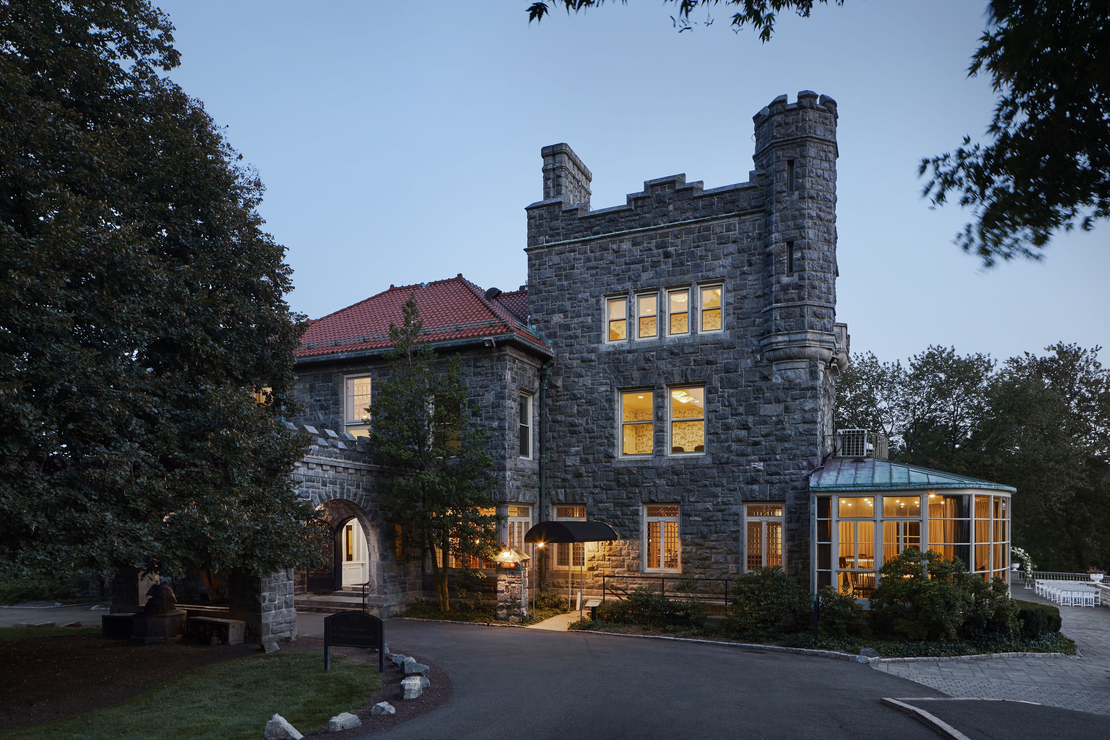 A stone building with a red-tiled roof, a turret, and a conservatory.