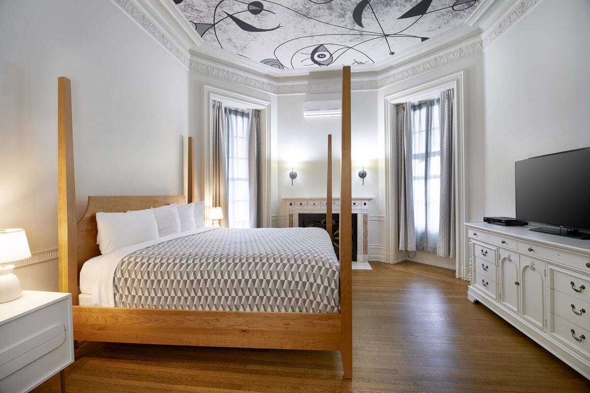 Een slaapkamer met een houten bed, een televisie op een kastje en een open haard op de achtergrond.