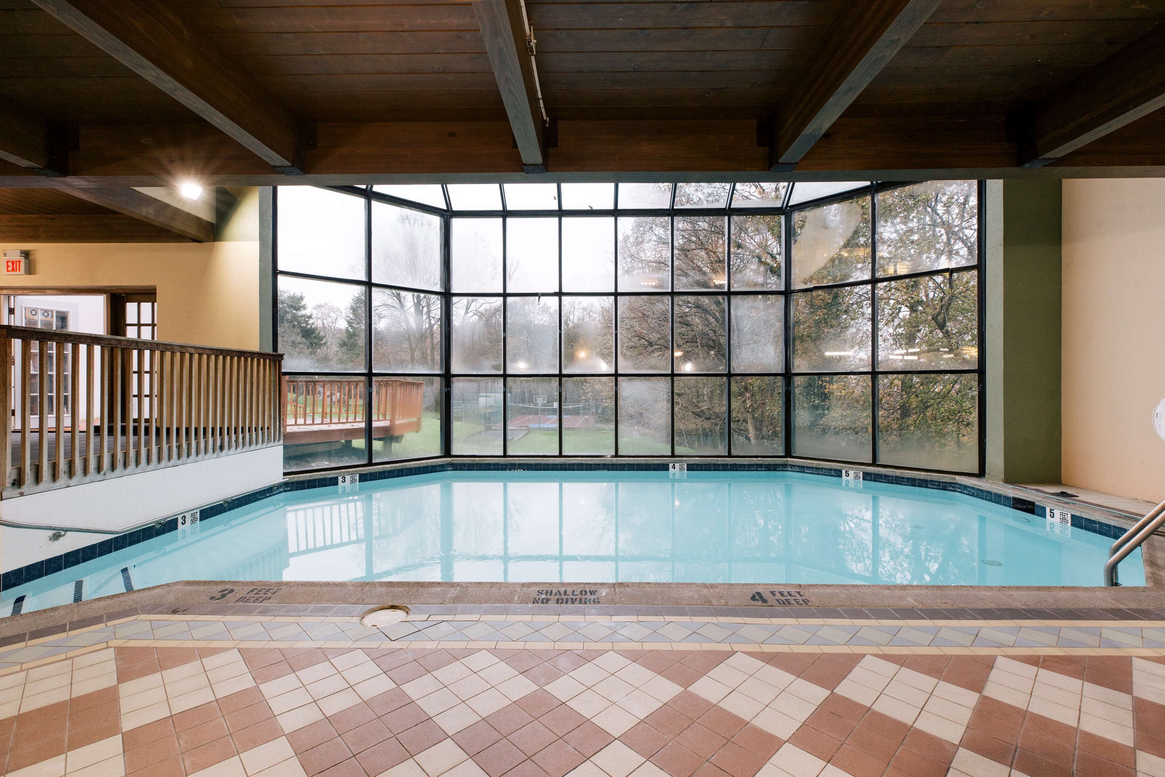 Une piscine intérieure avec de grandes fenêtres donnant sur la verdure, un sol carrelé et un plafond en bois.