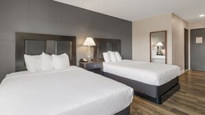 Una habitación de hotel con dos camas, una mesita de noche con lámpara, un espejo y una puerta.