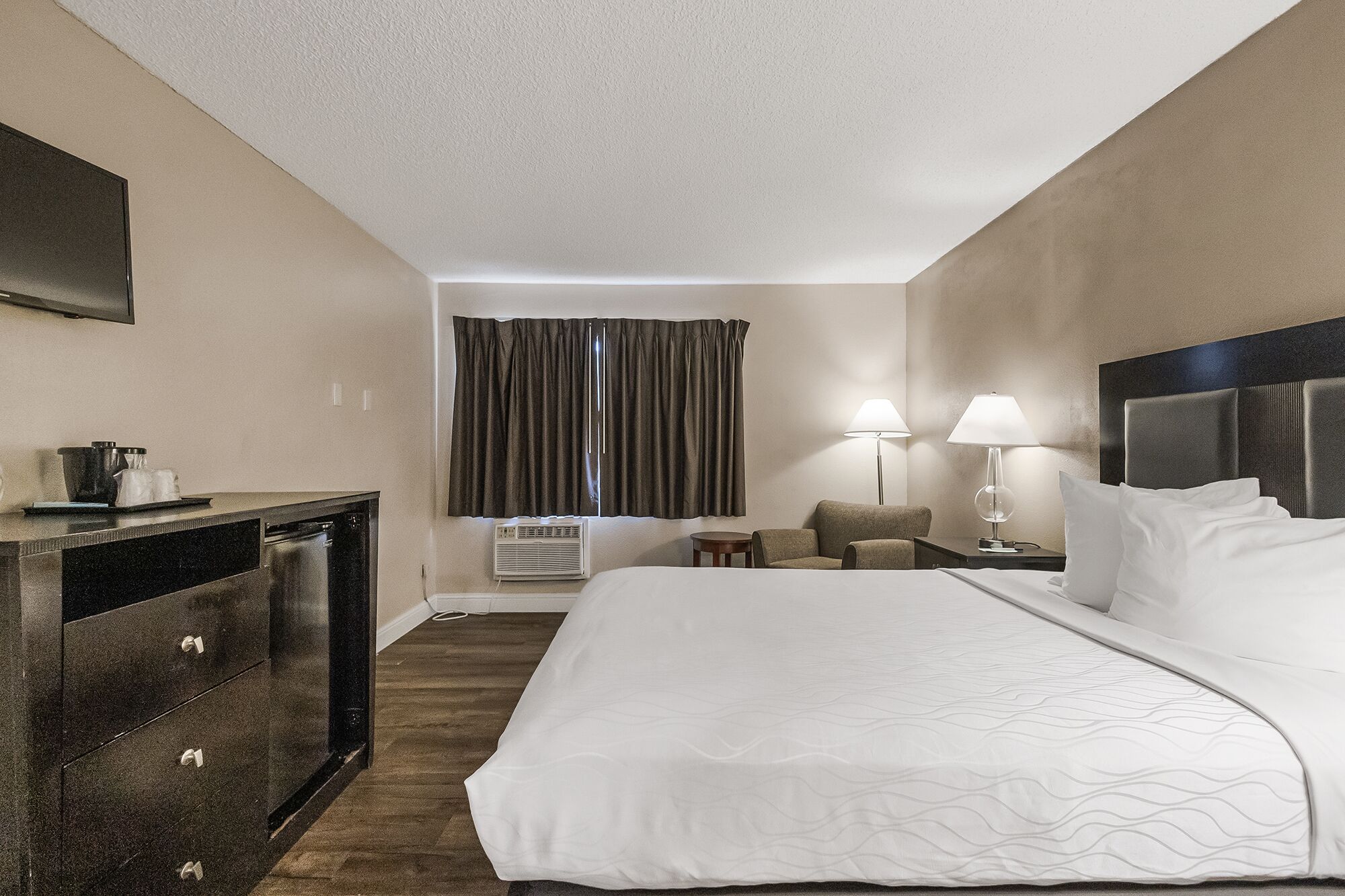 A hotel room with a bed, a desk, a chair, a lamp, and a television.