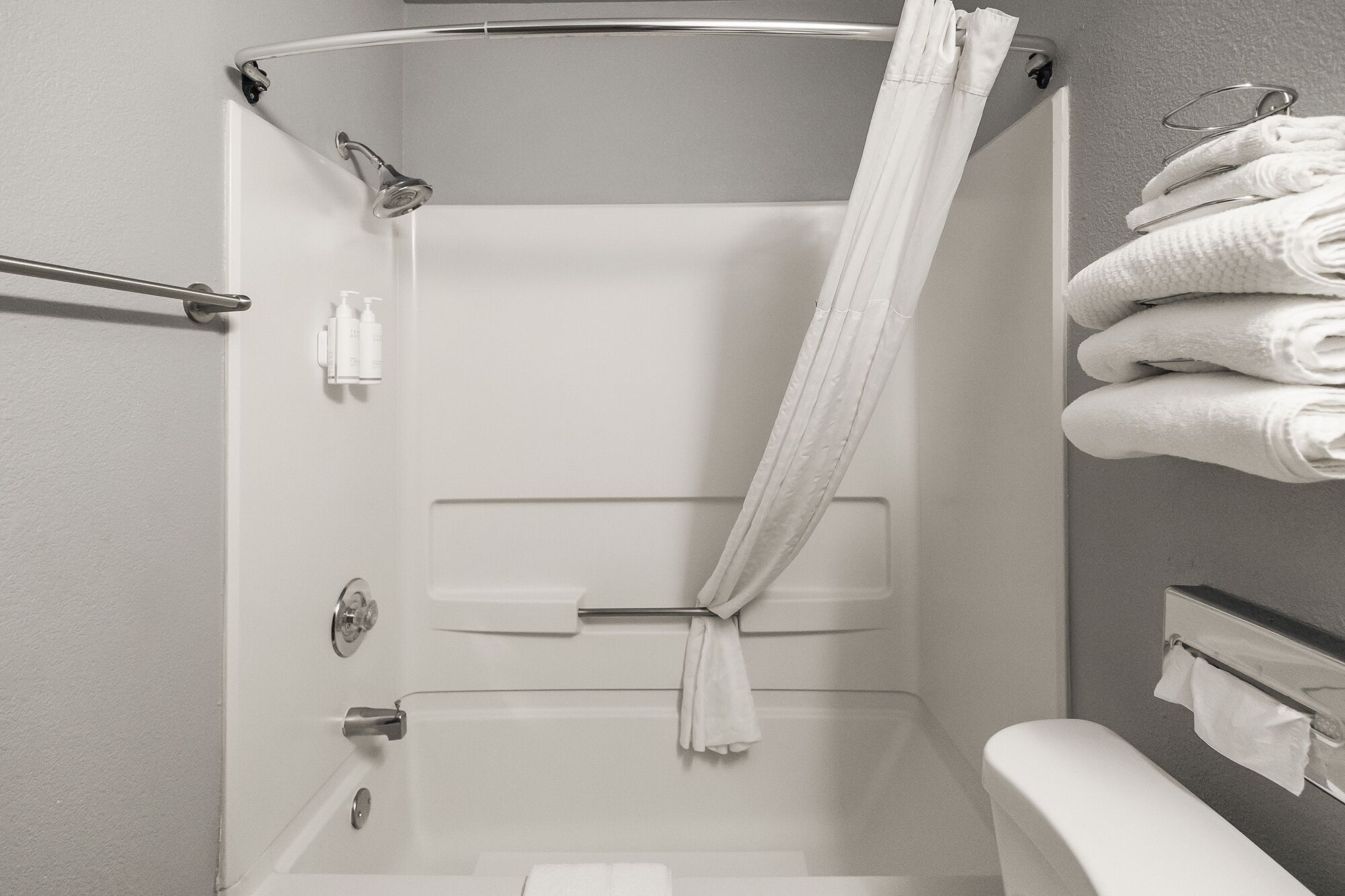 A shower with a curtain, a towel rack with towels, and toiletries on the wall.