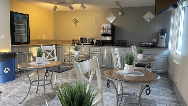 Una cocina moderna con encimeras de granito, armarios blancos y un comedor con mesas y sillas redondas.