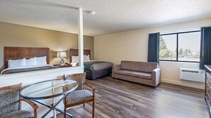 Una habitación de hotel con una cama, un sofá, una mesita de cristal y una silla.