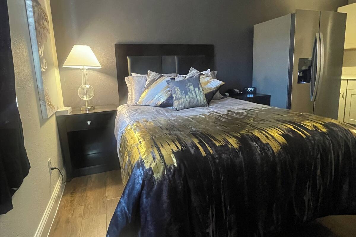 Quarto com cama, mesa de cabeceira, luminária, espelho e geladeira.