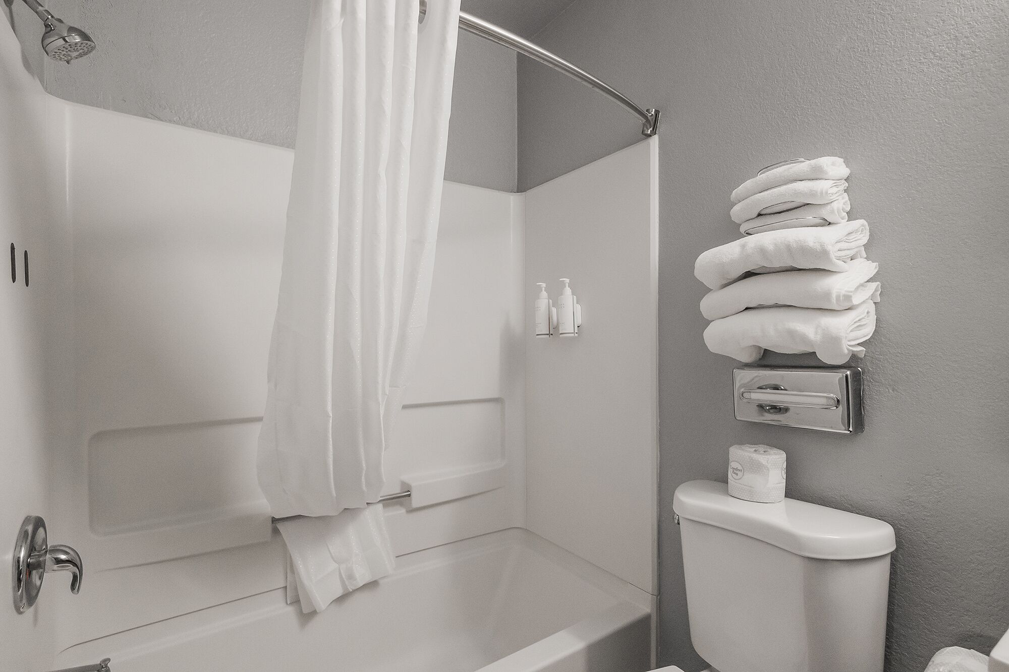 A bathroom with a bathtub, shower curtain, towel rack, toiletries, and a toilet.