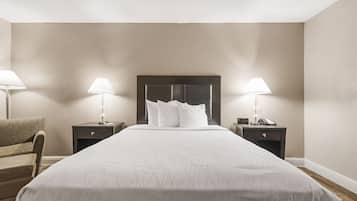 Een hotelkamer met een groot bed, twee nachtkastjes met lampen, een stoel en een donker hoofdeinde.