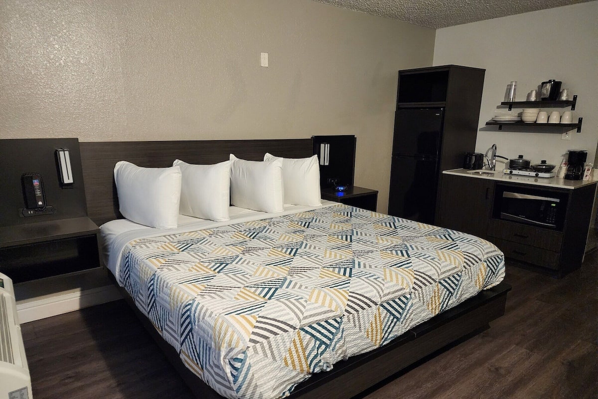 A hotel room with a large bed, a small kitchenette, and a dark wood floor.