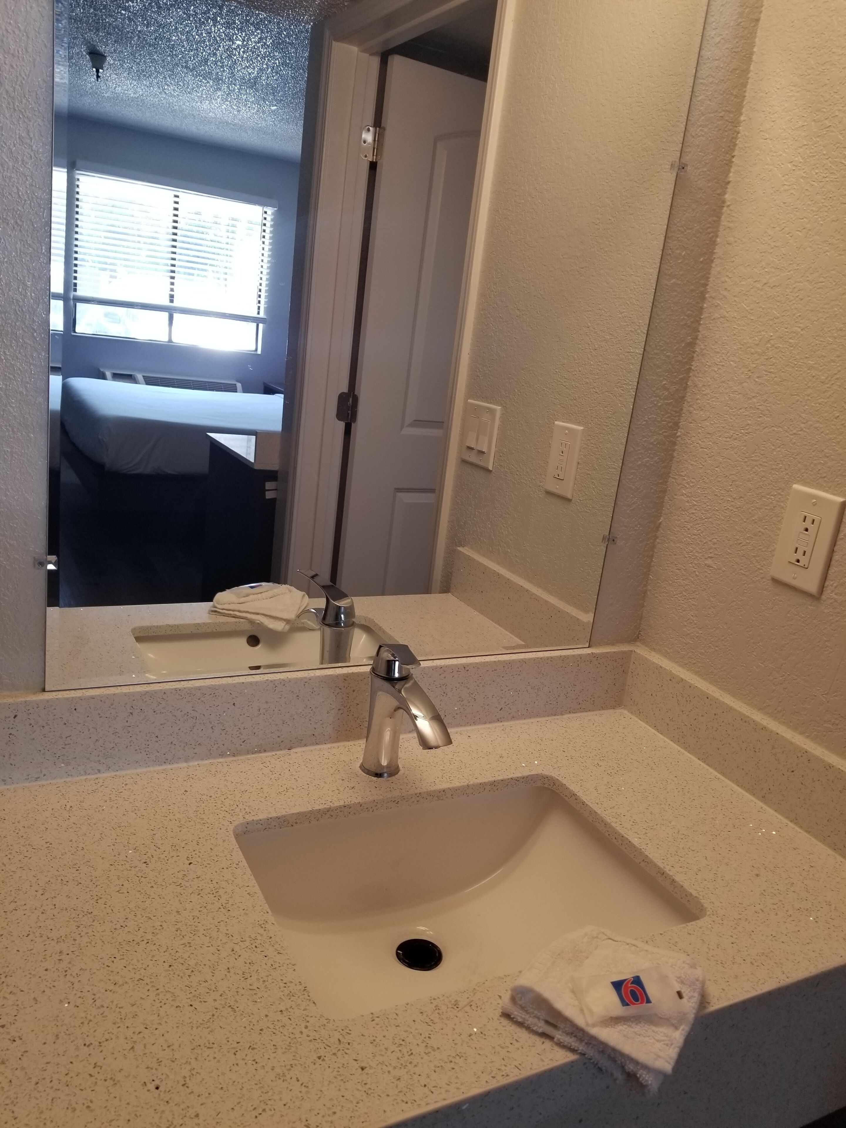 A bathroom with a sink, mirror, and a door leading to a bedroom.