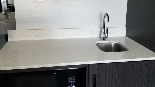 A modern kitchen with a built-in dishwasher, a stainless steel sink, and two black hanging shelves above the countertop. - Studio 6 Sacramento, CA - Natomas & SMF Airport (Sacramento)