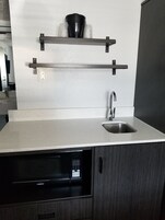 Una cocina moderna con lavavajillas empotrado, un lavamanos de acero inoxidable y dos estantes negros suspendidos sobre la encimera.