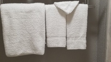 Een badkamer met een toilet, een handdoekhouder met meerdere witte handdoeken en een glazen plank boven het toilet.