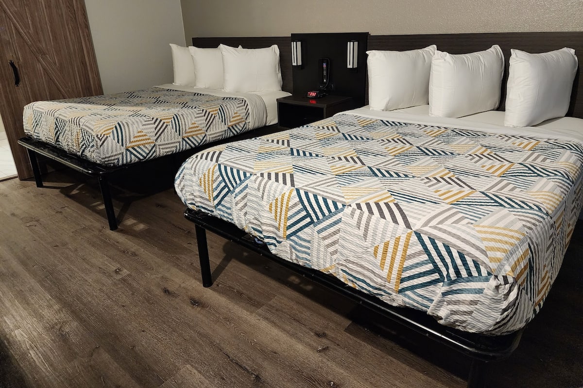 Two beds with patterned bedding, a nightstand with a clock, and a wooden floor.